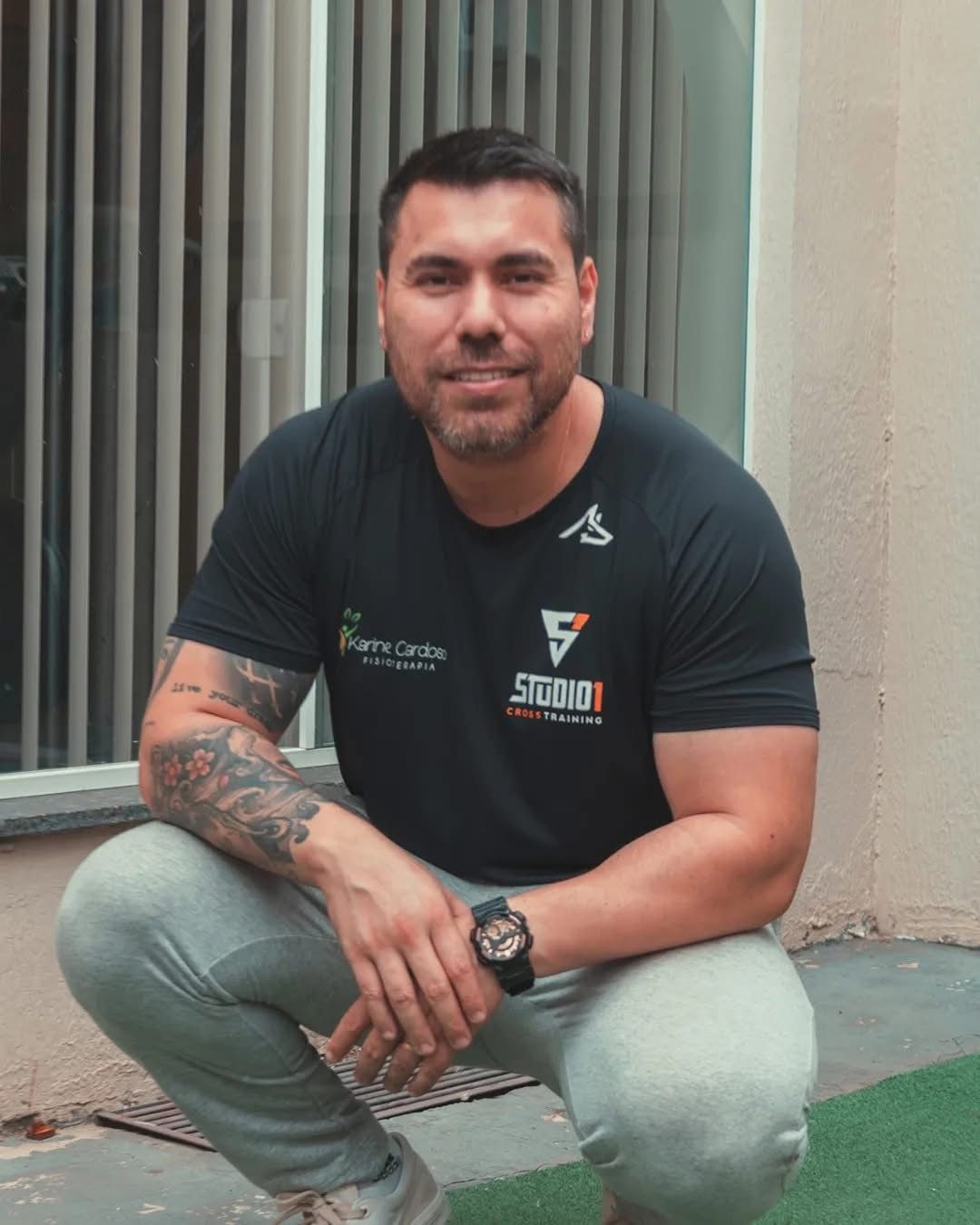 Diego Fioravante sorrindo, agachado em frente ao estúdio